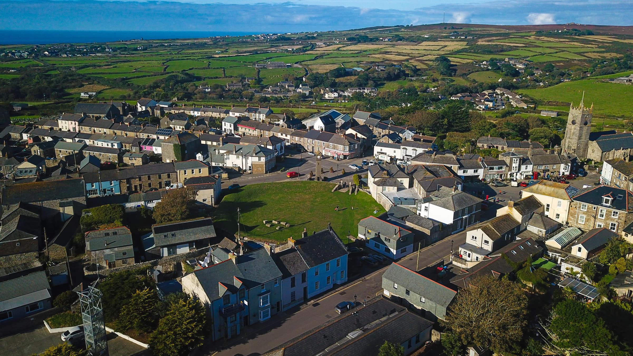 Aerial view over the rooftops of St Just to the church tower, with the moors of West Penwith beyond