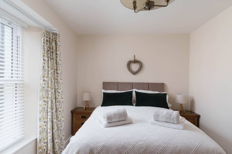Double bedroom with upholstered headboard, green velvet cushions and floral curtains