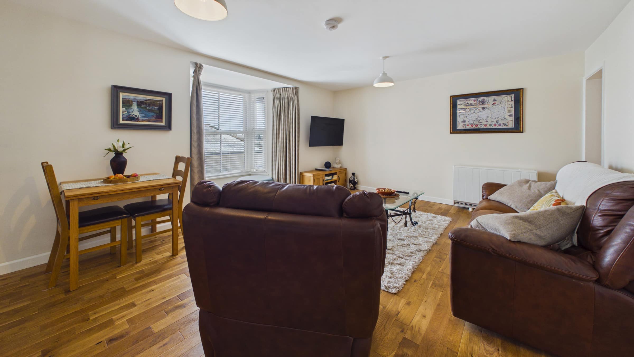 Open-plan living room of the First Floor Apartment with leather sofas, dining table and bay window
